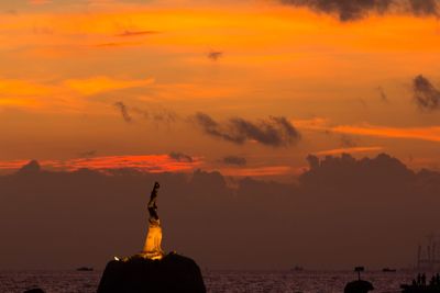 Silhouette statue by sea against orange sky