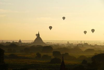 Hot air balloons flying over landscape against sky during sunset