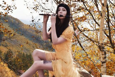 Portrait of woman playing flute while sitting on rock against mountain