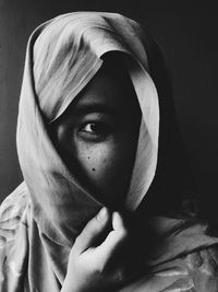 Close-up portrait of young woman wearing scarf against black background