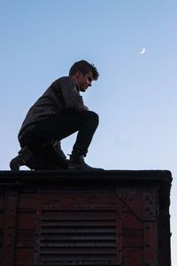 Low angle view of young man standing against clear sky