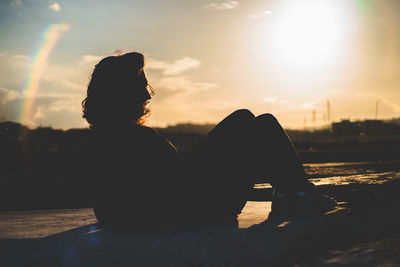 Side view of silhouette young woman sitting against sky during sunset