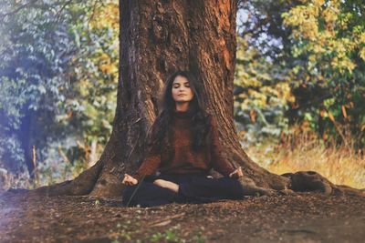 Full length of young woman practicing yoga against tree trunk in forest