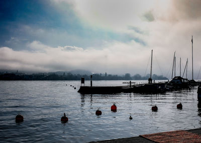 Sailboats moored in sea against sky