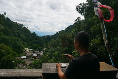 Rear view of man sitting on mountain against sky