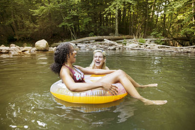 Cheerful female friends laughing using inner tubes in river