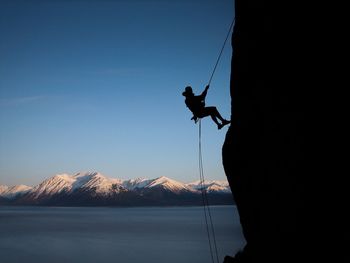 Silhouette man climbing mountain against clear sky