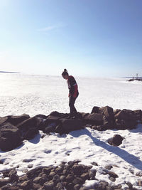 Side view of woman standing on rock by froze sea against sky