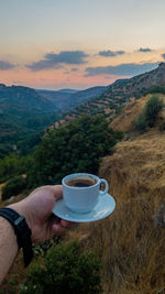 Man holding coffee cup against mountains and sky