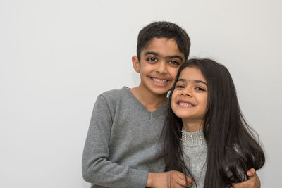 Portrait of smiling siblings standing against white background