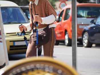 Midsection of man holding canes while walking on street against cars