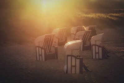 Hooded chairs on beach against sky during sunset