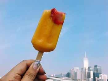 Cropped image of woman holding ice pop against sky