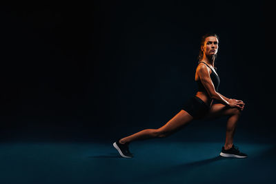 Full length of young woman exercising against blue background