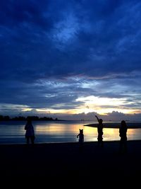 Silhouette people on beach against cloudy sky during sunset