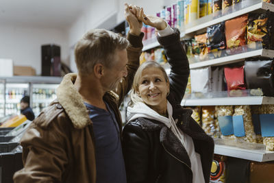 Happy mature couple dancing together with hand raised while shopping at supermarket