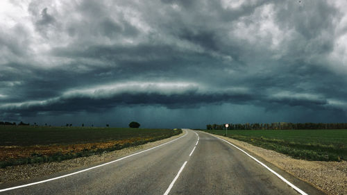 Road passing through field against sky