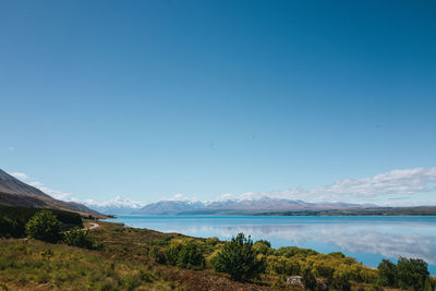 Scenic view of sea and mountains against clear blue sky