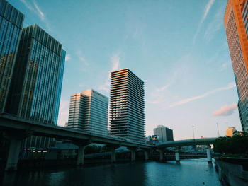 Modern buildings by river against sky in city