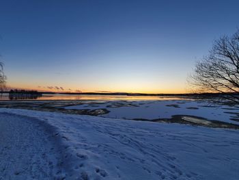 Snow covered landscape against sky during sunset