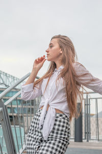 Thoughtful woman standing on steps against clear sky