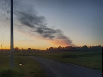 Road amidst field against sky during sunset