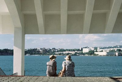 Rear view of woman standing by sea against cityscape