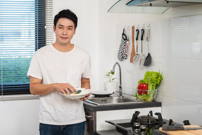 Portrait of young man using mobile phone while standing in kitchen