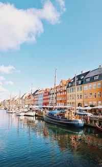 Sailboats moored on canal by buildings against sky