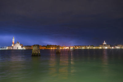 Illuminated buildings by river against sky in city at night