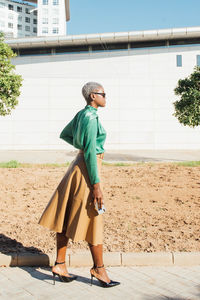 Side view of confident african american woman with shirt hair in stylish clothes and sunglasses standing on walkway on street in sunny day