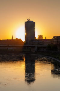 Bridge over river by buildings against clear sky during sunset