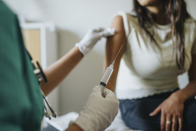Midsection of female doctor giving vaccine to young woman in clinic