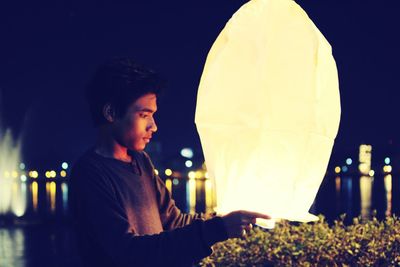 Young man holding illuminated paper lantern during diwali at night