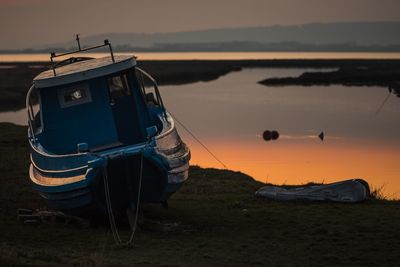 Boat moored on beach against sky during sunset