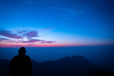 Rear view of silhouette man standing on mountain against sky