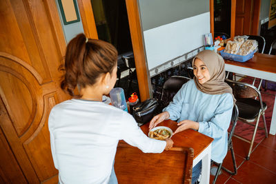 Rear view of mother and daughter sitting on sofa at home