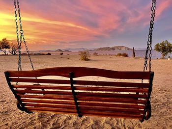 Empty deck chairs on beach against sky during sunset