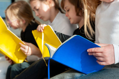 Four children sitting comfortably together on sofa in living room and doing prep work for school