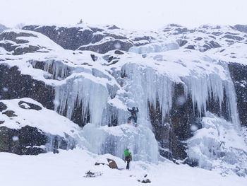 People climbing snow covered mountain during snowfall