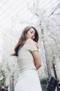 Low angle view of young woman standing against flowering trees at park