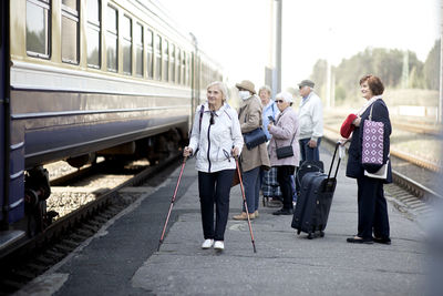 Positive elderly seniors people with face masks waiting train before traveling during a pandemic