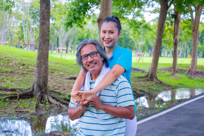 Portrait of smiling woman exercising with man against trees in park