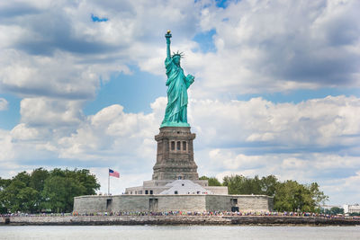 Low angle view of statue of liberty by river against cloudy sky