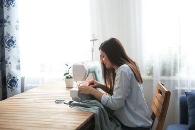 Charming girl with long black hair sews on a sewing machine, concept handmade and mother on