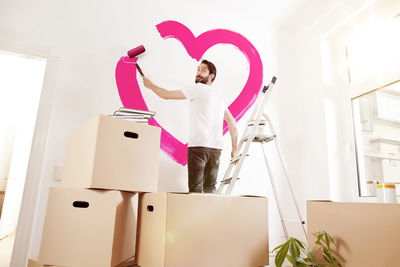 Young man painting a pink heart on a wall in new apartment