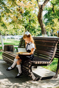 A child is sitting on a bench outside on a warm sunny day, and is returning to school. 