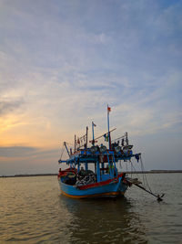 Fishing boat moored in sea against sky during sunset