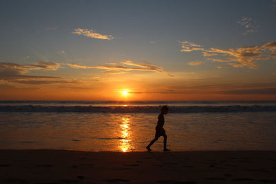 Silhouette boy walking at beach against sky during sunset