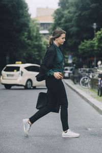 Side view of creative businesswoman crossing street in city